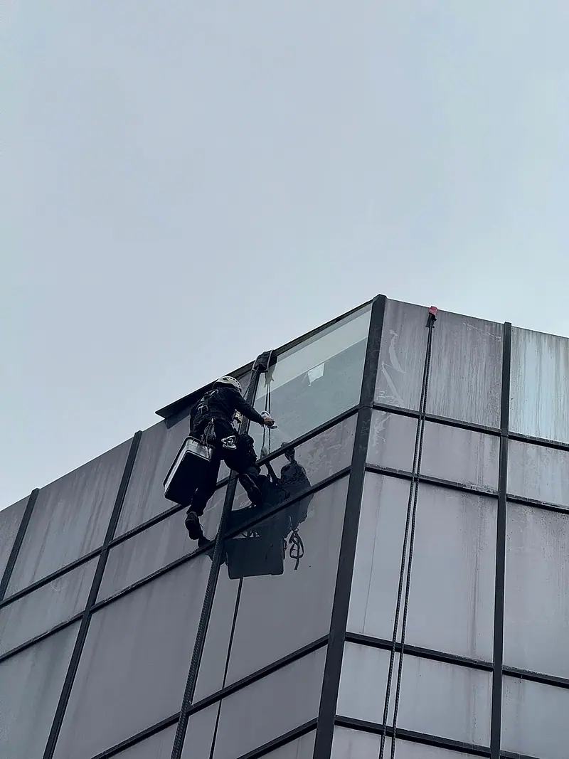 Technician on ropes at the corner of a dark glass building
