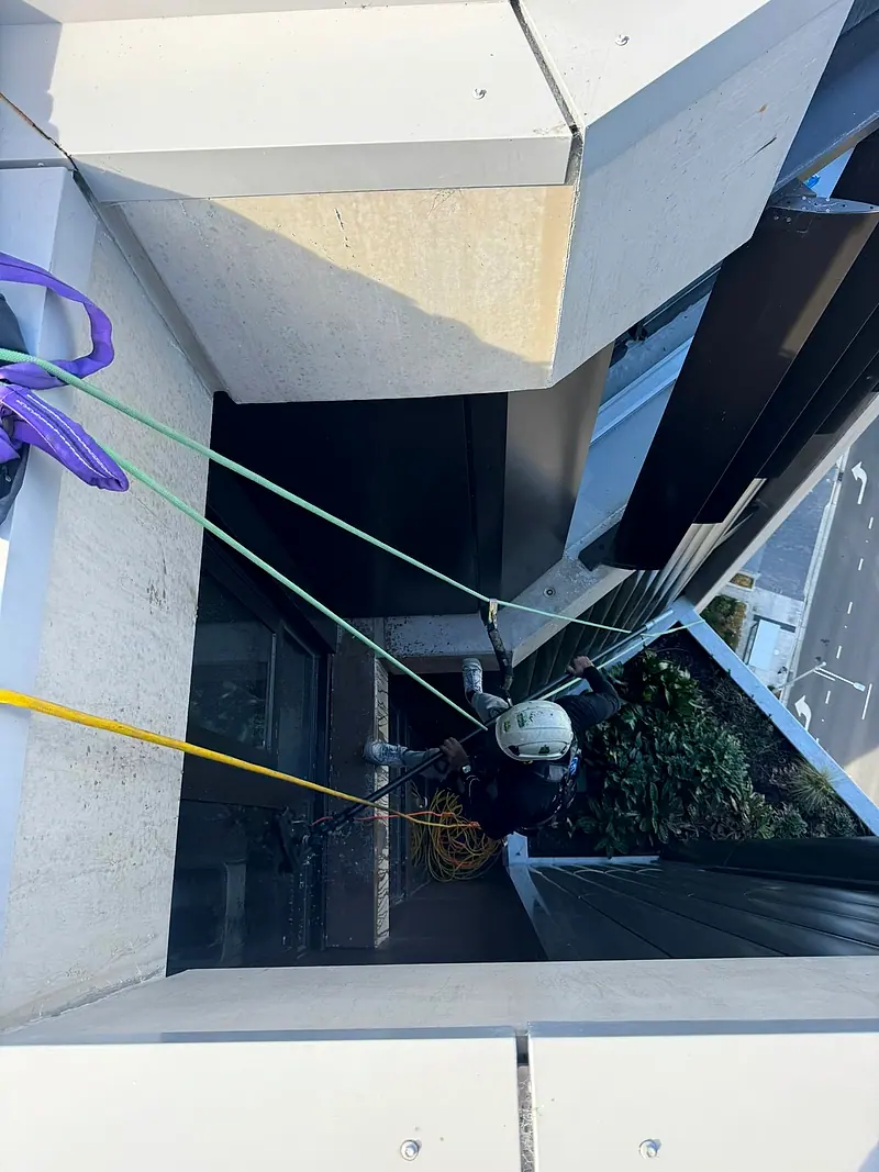 Technician on ropes working below a building ledge, seen from above