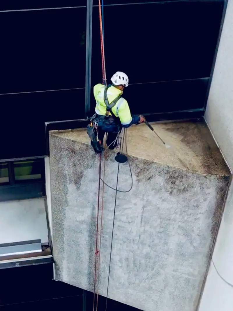 Technician pressure washing a concrete wall on rope access
